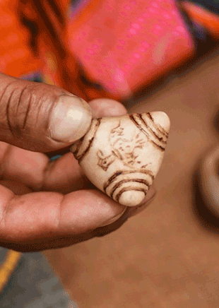 Chumpi-mesa-training | green tara college Close-up of a small carved bead held between a thumb and finger.